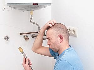 Confused-looking man stares at plumbing part and scratches his head