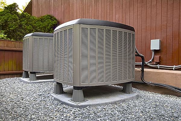 Outdoor heating and cooling system on stand above yard of rocks. Plugged into the side of a house.