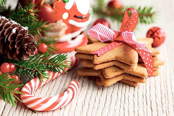 Holiday decorations, including pine, pinecone, berries, a Santa figurine, a candy cane, and several star-shaped cookies tied in a bow