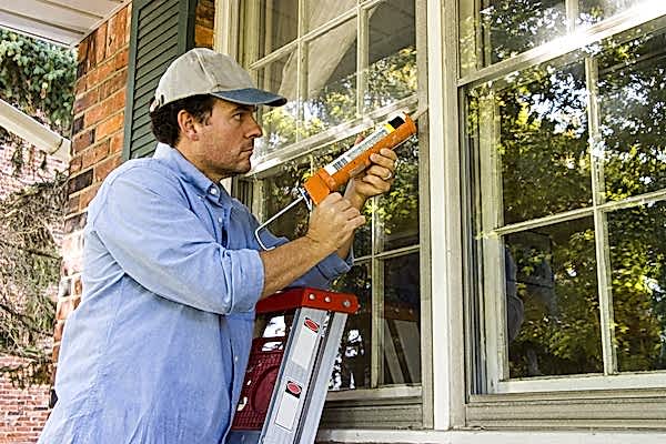 Man on ladder using caulking gun to seal window