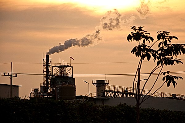 Factory in California's chimney giving off white smoke against orange sunset 