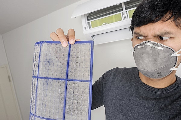 Man in face mask holding dirty air filter and looking at it with disgust