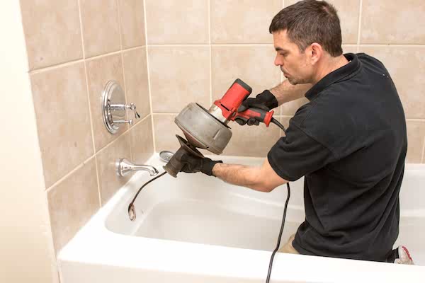 Plumber using auger on bathtub