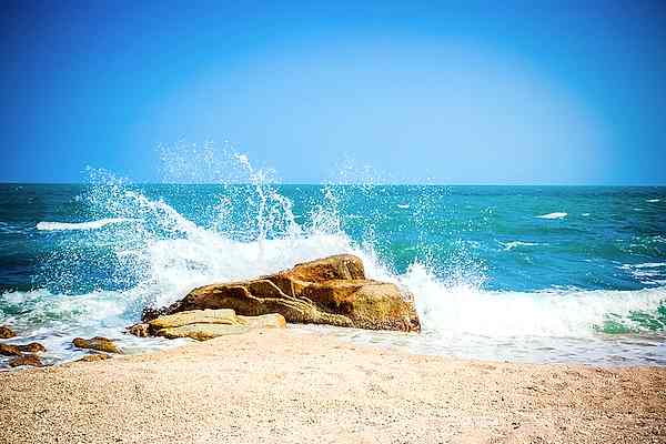 Waves breaking on a brown rock near a shoreline on a bright day. Water hammer.