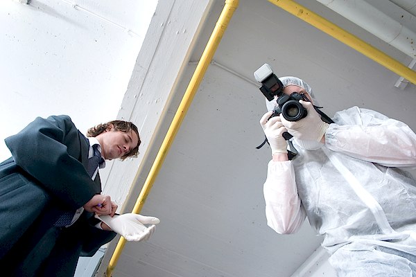 Two forensic detectives taking detailed notes and collecting photographic evidence of a crime scene
