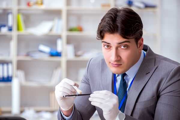 Man in suit wearing surgical gloves dusts a pen with a forensic brush