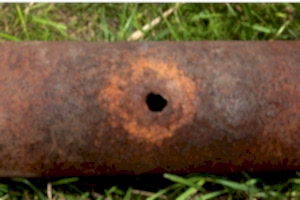 A hole rusted into an iron pipe.