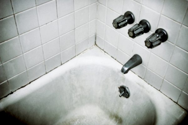 A white tiled shower with dark mold stains.