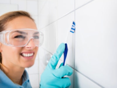 A woman scrubs mold from shower grout with a toothbrush.