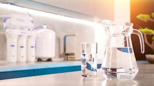 A pitcher of clean water in front of a reverse osmosis water filtration system.